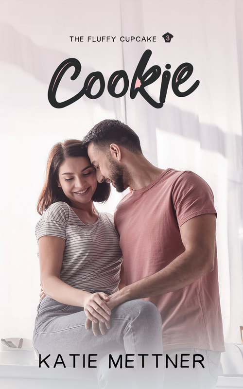 The book cover for Cookie, The Fluffy Cupcake Book 3, by katie mettner. There is a couple with their heads touching. He's wearing a pink shirt and has a dark beard and dark hair. She's wearing a striped shirt and has brown hair that is bobbed. She is sitting on the counter in front of windows.