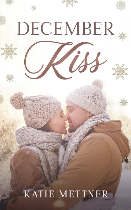 A couple in winter coats are embracing. There are snowflakes in the background. It says, "December Kiss, Katie Mettner"